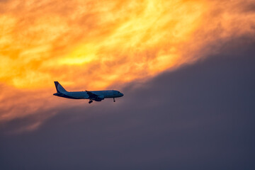 Airplane landing on orange cloudy dramatic sunset. Travel concept.