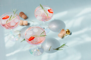 Summer drink with white sparkling wine. Homemade refreshing fruit cocktail or punch with champagne, strawberries, ice cubes and rosemary on light background.