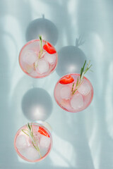 Summer drink with sparkling wine. Homemade refreshing fruit cocktail or punch with champagne, strawberries, ice cubes and rosemary on light blue background.