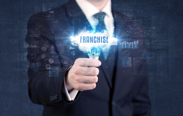Businessman holding a light bulb with FRANCHISE inscription, new business concept