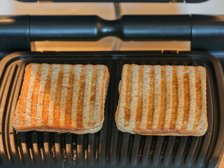 Toasted bread slices on the electric grill. Delicious toasted bread after roasting. Stripes on the...