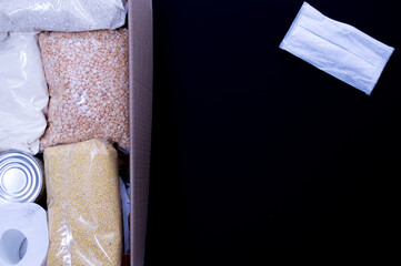 Cardboard box with Food supplies crisis food stock for quarantine and medical mask on the black background. Rice, canned food, toilet paper. Food delivery. coronavirus quarantine concept. Copyspace