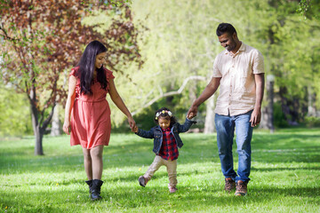 Father, mother and two years old girl are walking in sunny spring park