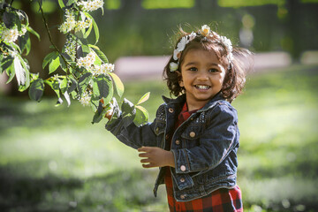 A two years old girl in park at a blooming branch of bird cherry tree - 362235360