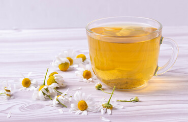 herbal fresh hot tea in a glass cup and camomile flowers