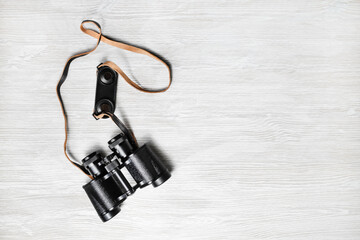 Photo of vintage black binoculars on light wood table background. Copy space for your text. Flat lay.