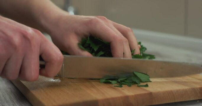Caucasian female hands cut with knife fresh parsley on wooden cutting board.