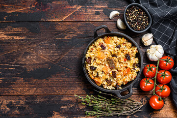 Pilaf in a pan. Central Asian cuisine Plov.  Dark wooden background. Top view. Copy space