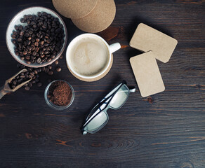 Obraz na płótnie Canvas Still life with coffee cup, kraft business cards, coffee beans, glasses and ground powder on old wooden background. Top view. Flat lay.