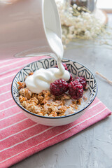 Yogurt is poured onto muesli in a plate 