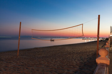 Volleyball net on the beach at sunset with the sea on the background.
