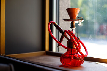 A small red hookah stands on a shelf, against the window, smoky bar, rest, tobacco, smoking,...