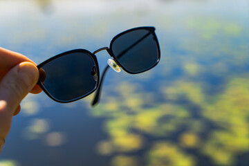 Sunglasses in hand in Sunny weather against the background of water.