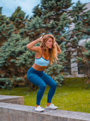 Fitness session with a young blonde caucasian woman doing exercise in a park with a blue maya on her feet and a white short shirt. Squatting