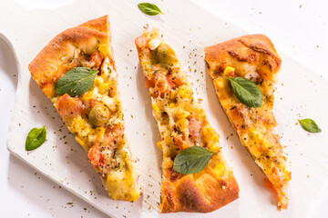 Três pedaços de pizza portuguesa com folhas de manjericão sobre a tábua branca