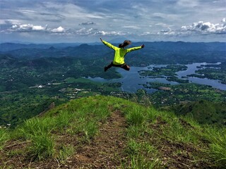 Hiking hiker jumping on the top of a mountain with a blue sky and river on the background 