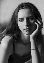 Obraz premium A sad girl with bare shoulders props her face with her hand. Dramatic image. Spectacular monochrome woman portrait.