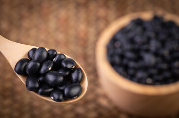 ฺBlack beans in a wooden spoon with Black beans in a wooden cup placed on a bamboo weave.