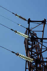 Electricity pylon with insulators and power lines. Blue sky background. Rusty weathered metal
