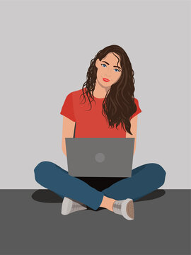 Young woman working on laptop computer while sitting on the floor with legs crossed isolated over gray background