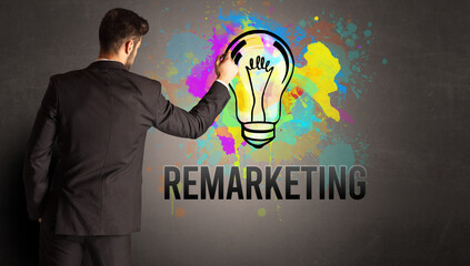businessman drawing colorful light bulb with REMARKETING inscription on textured concrete wall, new business idea concept