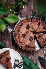Hommade chocolate berry fruit pie on wooden background with green leaves, summer pie outdoors, piece of pie on the plate