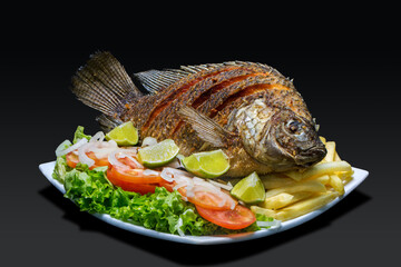 Fried whole fish with tomato and onion salad, on black background