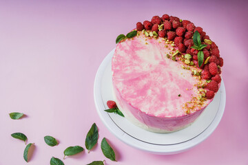 Celebratory cake with pink cream on a pink background. Cake decor made from fresh raspberries, crushed pistachios and mint. Green fresh mint leaves. Cake with raspberries. 