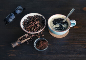 Photo of fresh tasty coffee on wooden background. Coffee cup, coffee beans, ground powder and glasses.