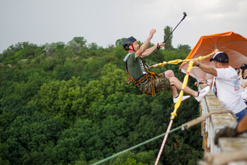 Concept of Extreme Sports and Fun. The man is a  thrill-seeker and a  rope jumper from the bridge. He is very happy to make a dream come true. He  is holding an action camera and insanely happy