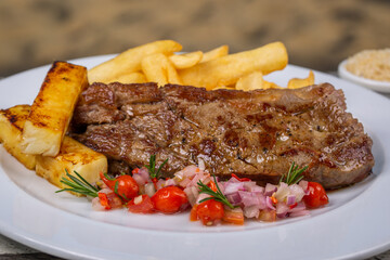 Delicious grilled steak beef with french fries, baked cheese and vinaigrette sauce on a white dish.with blurred background