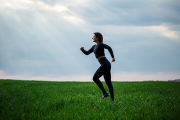 Fototapeta na wymiar Young attractive brunette woman standing in nature, wearing black leggings and a black top. Summer day, green grass. Athletic body and healthy lifestyle.