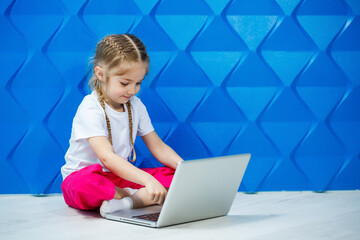 7 years old girl in a white T-shirt sits on the floor with a laptop and presses the keys