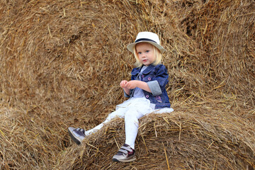 Naklejka na ściany i meble Portrait of a little girl on a haystack in summer