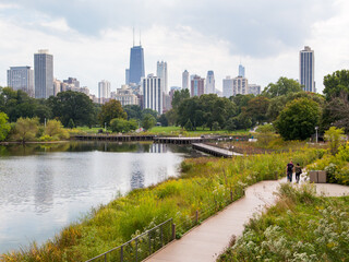 Naklejka premium Lincoln Park in autumn foliage with people walking in alleys and city skyline in the background, Chicago, Illinois