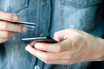Young man sat in the living room on sofa , using his phone, a smartphone and holding credit card her online To buy product in the internet