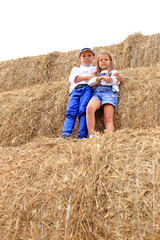 Naklejka na ściany i meble Two children are high under the sky on a haystack in the hay season.
