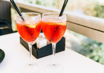 Closeup glasses of cocktail decorated with oranges on the table. Colorful pink soft drinks with ice and straws in a cafe. 