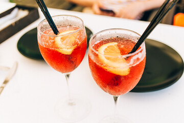 Closeup glasses of cocktail decorated with oranges on the table. Colorful pink soft drinks with ice and straws in a cafe. 
