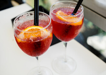 Closeup glasses of cocktail decorated with oranges on the table. Colorful pink soft drinks with ice and straws in a cafe. 