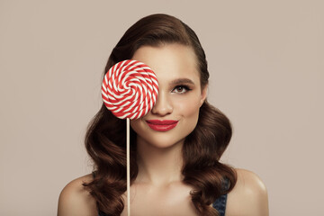 Smiling pin-up girl holding a big red lollipop in hand.