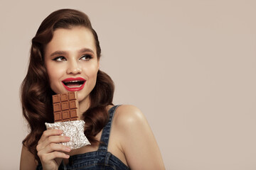 Cheerful pin-up girl holds a bar of chocolate in hand