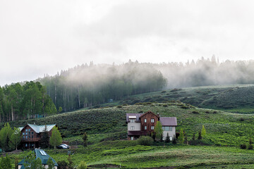 Obraz premium Crested Butte, USA Colorado small America town village in summer with clouds and foggy mist morning and houses on hillside with green trees