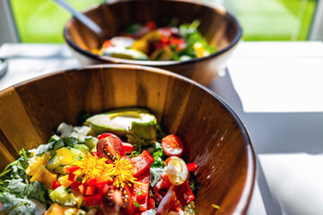 Closeup of two raw vegetable salad bowls with dandelion flowers on top of greens, red bell peppers and heirloom cherry tomatoes