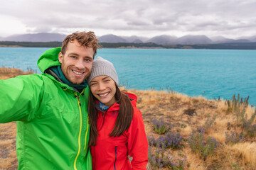 Naklejka premium New Zealand travel selfie happy couple backpackers hiking hikers taking phone self-portrait photo on blue lake nature background. Active healthy happy people.
