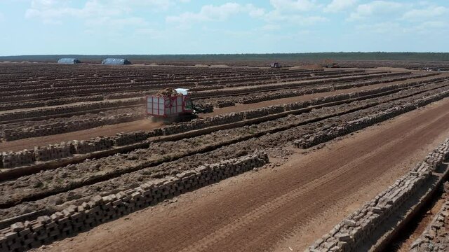Aerial view of industrial peatlands following a red tractor through peat production field. 4k footage. Close up of peat briquettes. Forward motion.