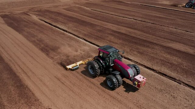 Aerial view following a red tractor working industrial peatlands. Peat production landscape. 4k footage. View from above. Backwards motion. Pan to right.