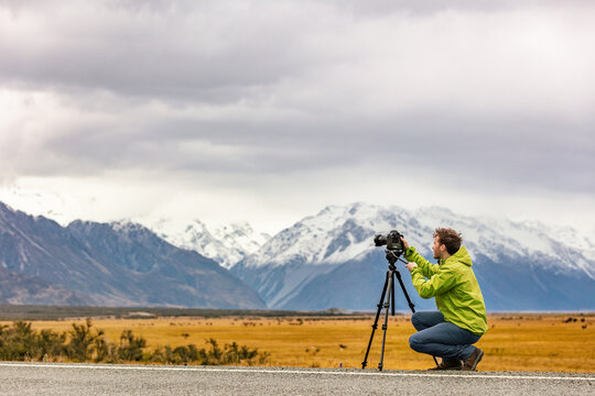 Tourist photographer taking pictures with professional camera on tripod on adventure travel vacation in New Zealand mountains landscape. - Powered by Adobe