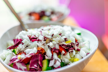 Vegan salad bowl with radicchio and chopped onions, cucumbers and endive lettuce chicory purple leaves for lunch or dinner and pink background
