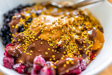 Macro closeup of oatmeal porridge bowl with peanut butter, chocolate sauce and blueberries with bee pollen as topping healthy vegetarian dish